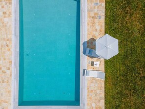 Une piscine rectangulaire bordée de carreaux, une zone herbeuse sur la droite et un parasol blanc.