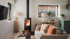 A cozy living room with a fireplace, a sofa, a coffee table, and a window with a view. - Longstones Avebury – Adam (Marlborough)