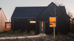 A modern two-story house with a dark exterior and a visible interior through a window. - Longstones Avebury – Adam (Marlborough)