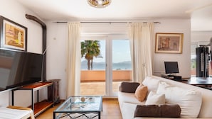 A living room with a sofa, TV, and a glass coffee table. - Villa 'La Gola' with Sea Views, Shared Pool and Wi-Fi (La manga)