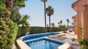 A swimming pool with a curved edge, surrounded by palm trees and greenery. - Villa 'La Gola' with Sea Views, Shared Pool and Wi-Fi (La manga)
