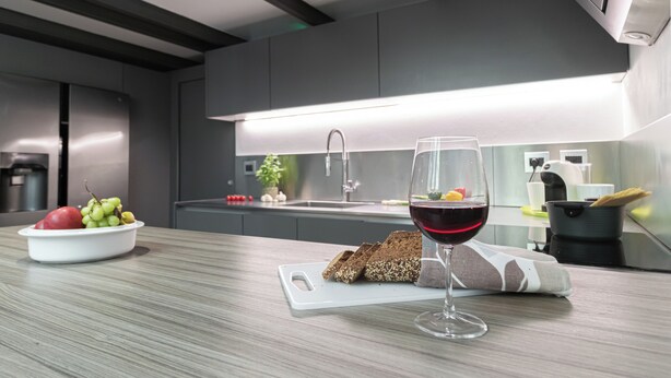 A modern kitchen with a white countertop, a bowl of fruit, a glass of red wine, and a loaf of bread. - Italianway Comfort - Mancini 3 (Milan)