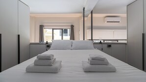 A modern hotel room with a large bed, two towels on the bed, a window with curtains, an air conditioning unit, and a view of the outside. - Italianway Comfort - Mancini 3 (Milan)