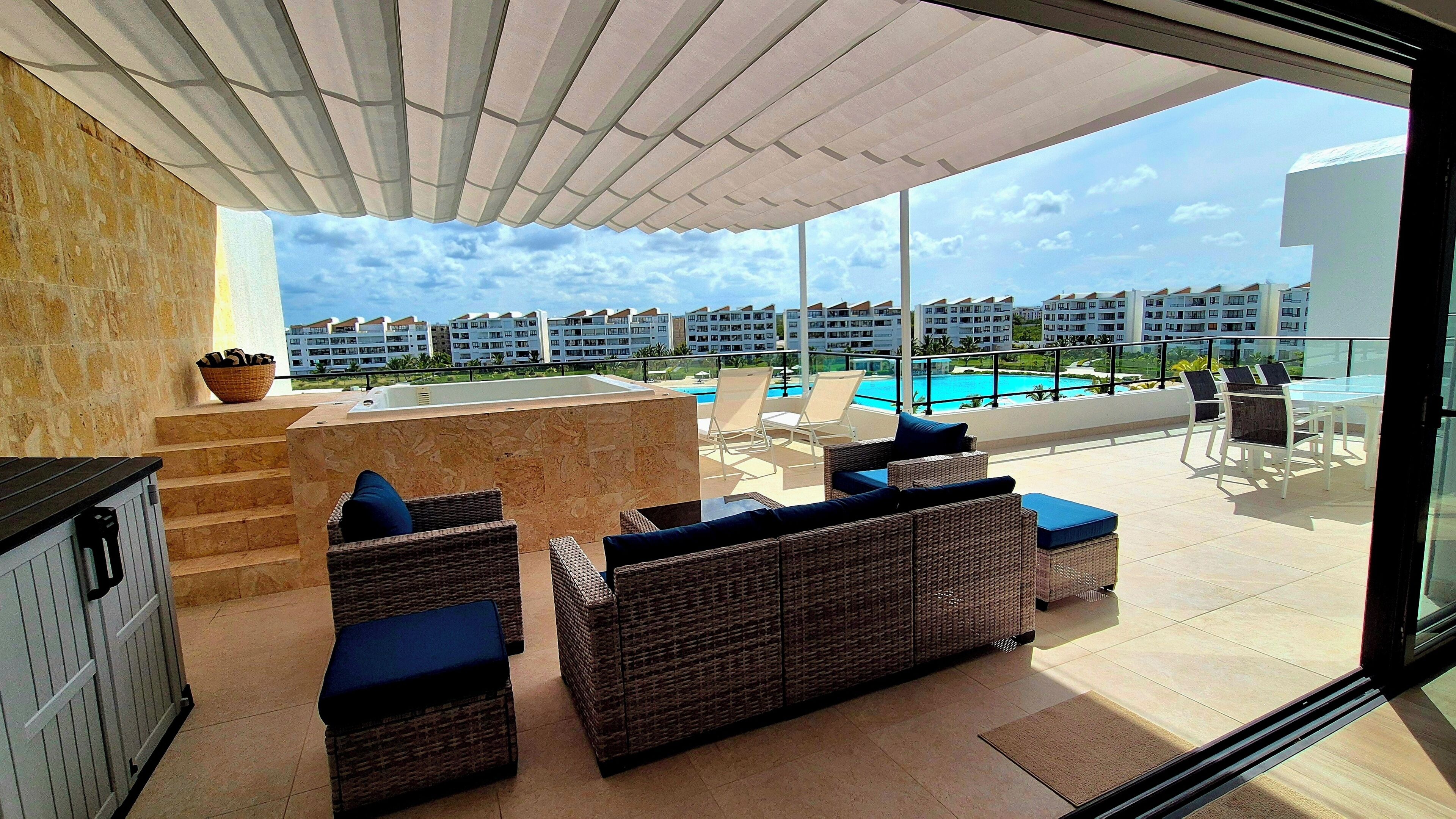 A balcony with wicker furniture, a pool, and a view of other buildings.