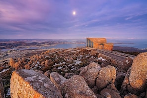 A modern building with large glass windows, situated on a rocky outcrop overlooking a coastal landscape.