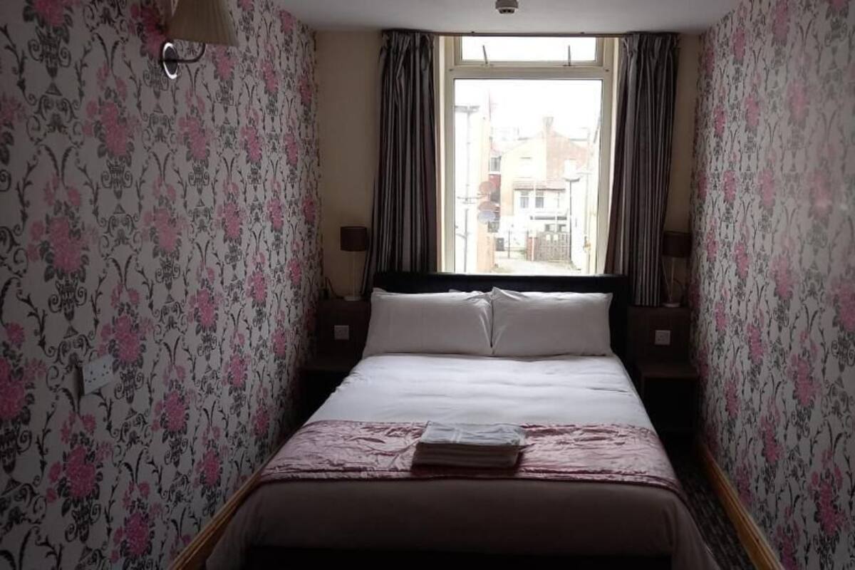 Una habitación de hotel con cama, cortinas, una ventana y vistas a edificios.