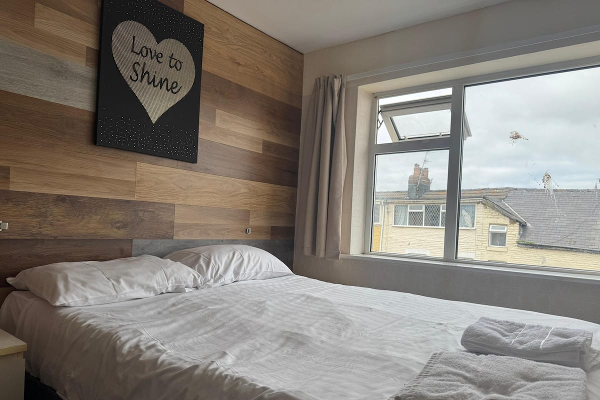 Una cama bien hecha con sábanas blancas y una obra de arte con forma de corazón en la pared.