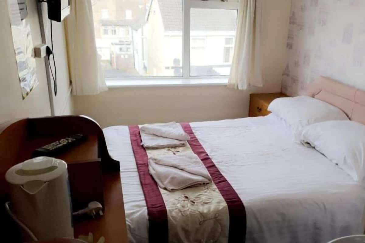 Una habitación de hotel con una cama, una mesita de noche, un control remoto y una ventana con cortinas.
