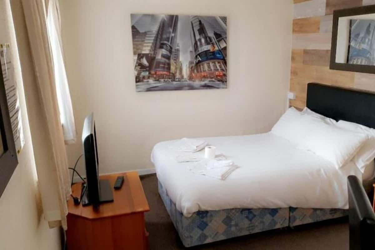 Una habitación de hotel con una cama, un escritorio con televisor y un cuadro en la pared.