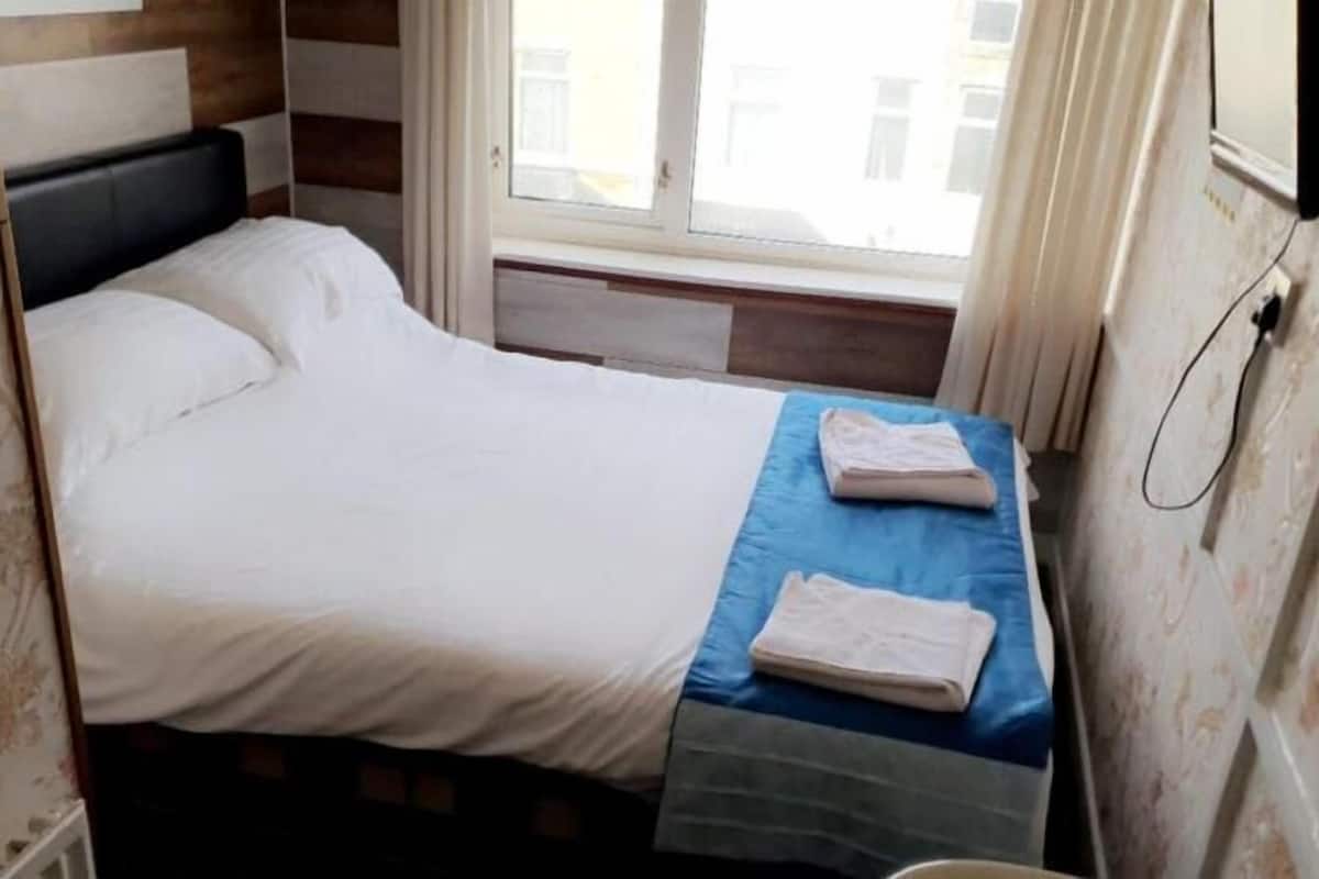 Un dormitorio con cama, ventana y televisor en la pared.