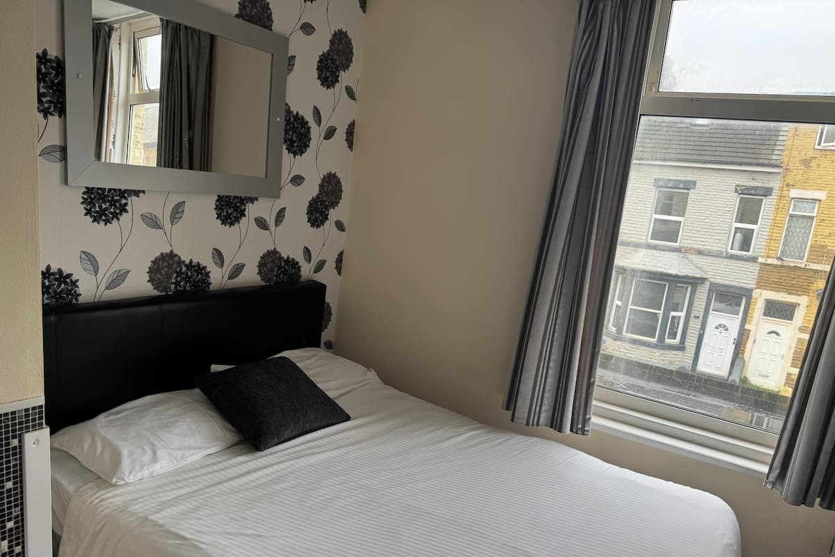 Habitación de hotel con cama, un espejo grande, papel tapiz floral y una ventana con vista a edificios.