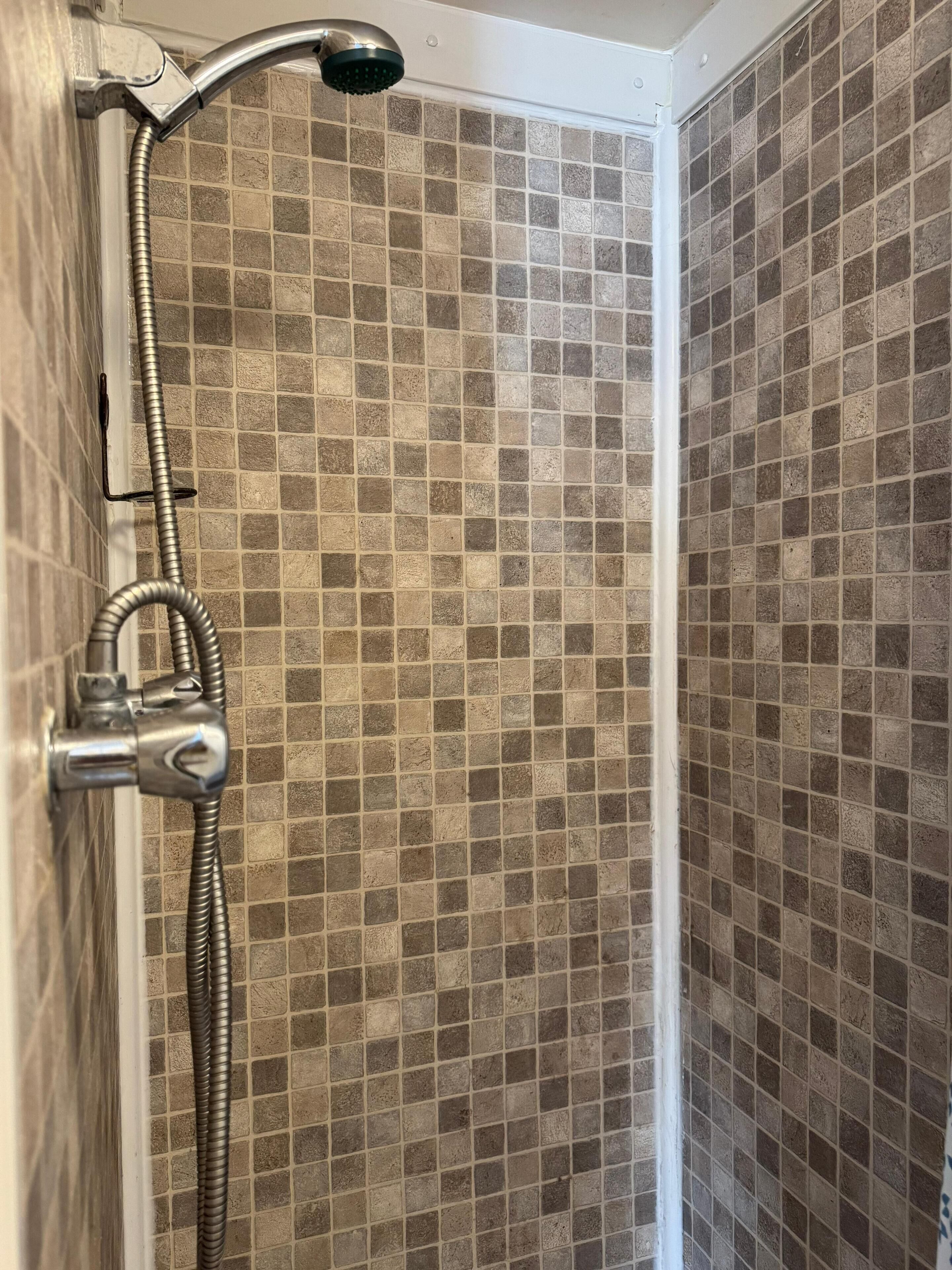 Een douche met een flexibele slang en een handdouche, betegelde wanden met een mozaïekpatroon.