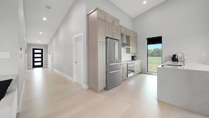 A modern kitchen with stainless steel appliances, a marble countertop, and a view of the outdoors. - New Modern Home in the Finger Lakes (Romulus)