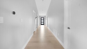 A long, narrow hallway with white walls and wooden flooring, leading to a door at the end. - New Modern Home in the Finger Lakes (Romulus)