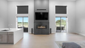 A modern kitchen with a central island, a built-in fireplace, and large sliding glass doors leading to an outdoor area. - New Modern Home in the Finger Lakes (Romulus)