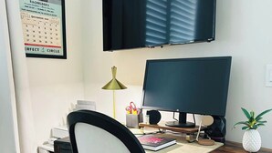 A home office setup with a desk, chair, computer, and a TV mounted on the wall. - 3-bedroom condo in charming Melbourne Beach with AC (Melbourne Beach)
