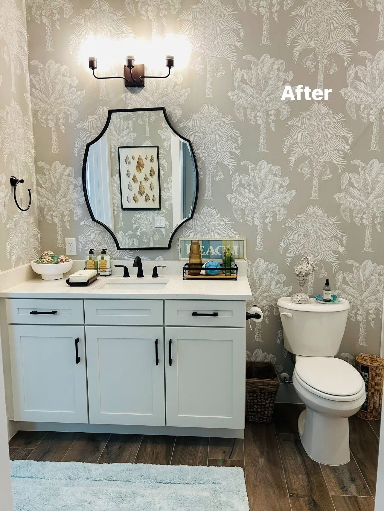 Un baño con tocador, espejo, inodoro y una pared con estampado de hojas tropicales.