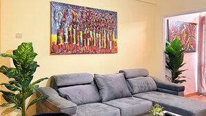 A modern living room with a grey sectional sofa, a glass coffee table, and a large abstract painting on the wall. - Charming T1 in Historical Building-2min to Luanda Bay Museums-Marginal (Luanda)