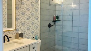 A bathroom with a patterned wallpaper, a white sink, a toilet, and a glass-enclosed shower area.
