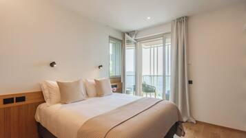 A bedroom with a large bed, a wooden headboard, a nightstand, and a view of the outdoors through a glass door.