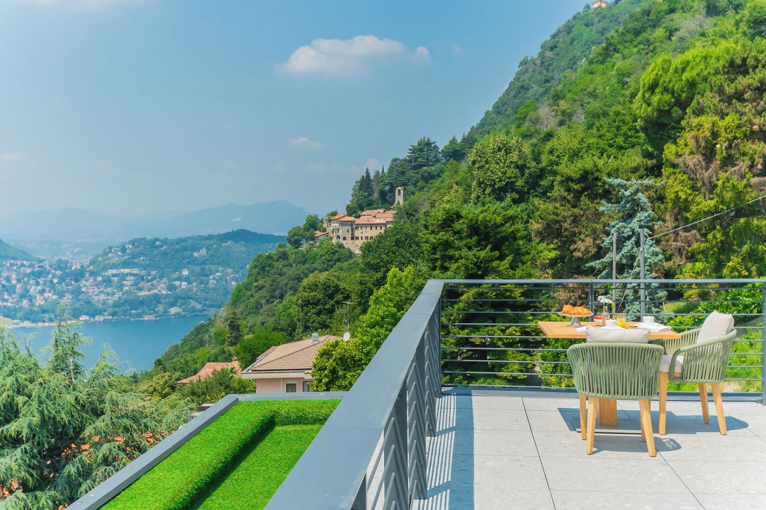 A terrace with a table and chairs overlooking a lake and hills.