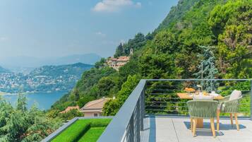 A terrace with a table and chairs overlooking a lake and hills.