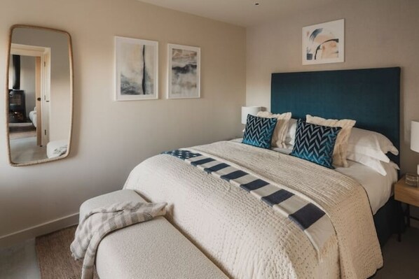 A bedroom with a large bed, a headboard, a bedside table, and a mirror.