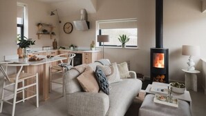 Ein gemütliches Wohnzimmer mit einer Couch, einem Couchtisch und einem Kamin. Es gibt eine Küchenzeile mit einem Esstisch und Stühlen.