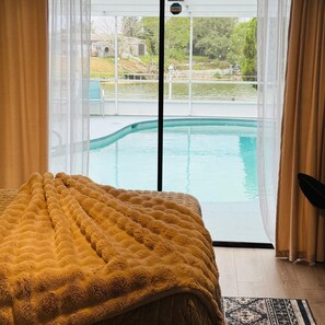 A bedroom with a bed, a view of a swimming pool, and a door leading outside.
