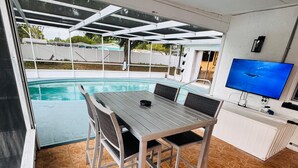 A covered outdoor dining area with a pool, a TV, and a white cabinet. - #55 The Lakeside Oasis Pool Home by Joyful Moments (Port Richey)