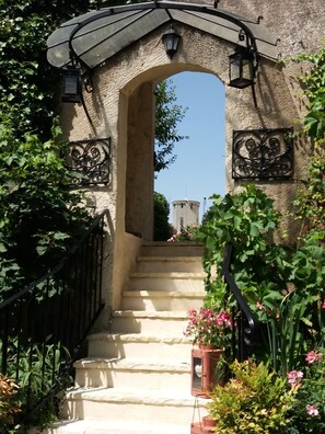 Un arc en pierre mène à un escalier qui offre une vue sur une tour en arrière-plan.
