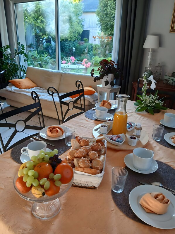 Una mesa de desayuno con frutas, pasteles y vistas a un jardín a través de una ventana.