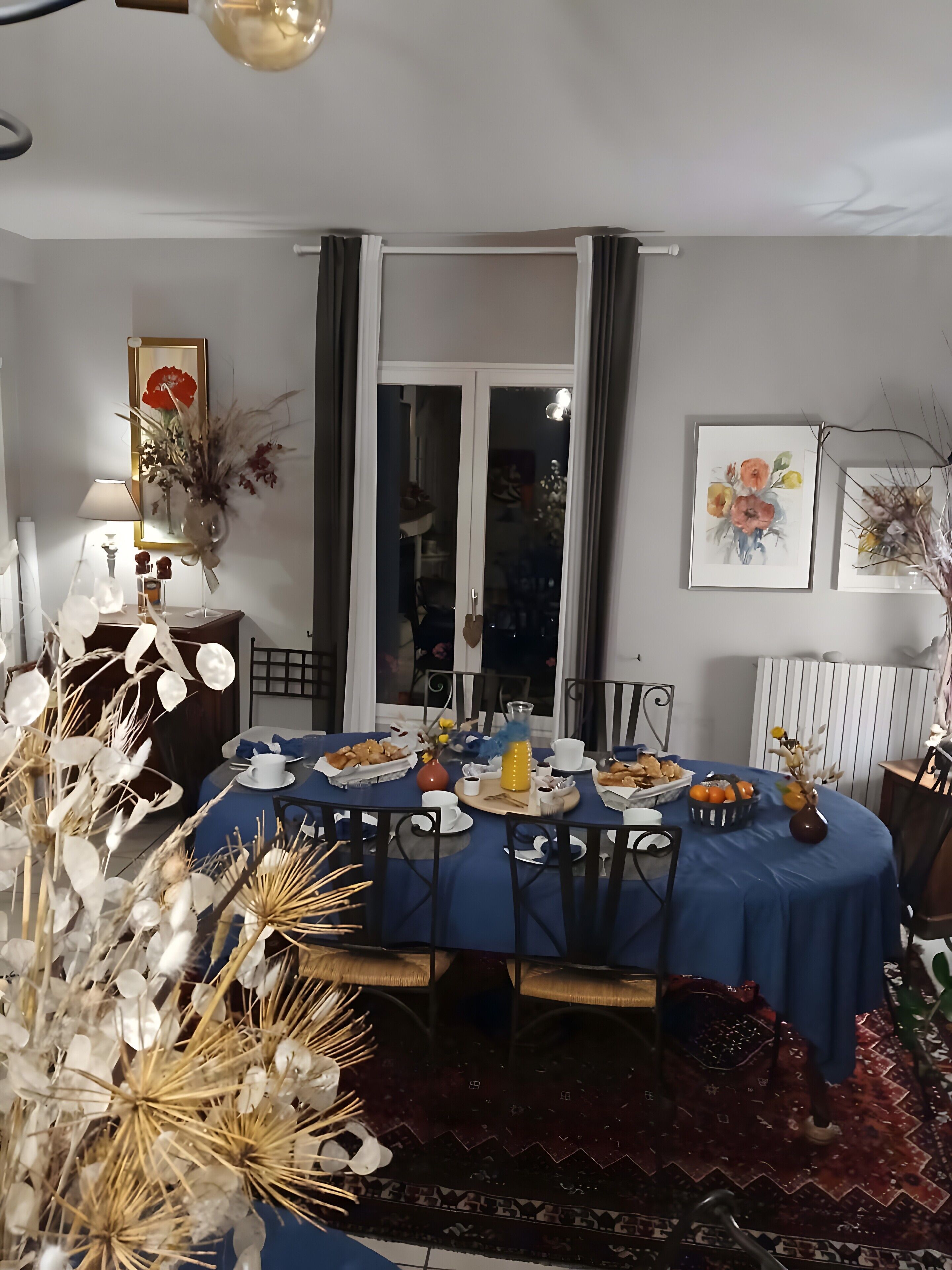 A dining area with a table set for four, a vase with dried flowers, and a framed picture on the wall.