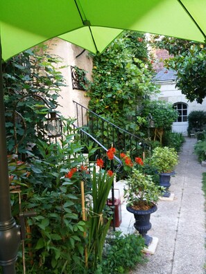 Un espacio al aire libre techado con una escalera, plantas en macetas y un edificio al fondo.