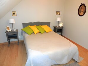 Ein Schlafzimmer mit einem Bett, zwei Nachttischen, einer Lampe auf jedem Tisch und einem Spiegel am rechten Nachttisch, sowie einem Bild an der Wand.