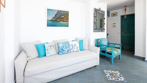 A white sofa with blue and white cushions, a blue chair, a painting of a coastal scene, and a mirror with a blue frame. - Villa Marea by My Villa Collection (Capri)