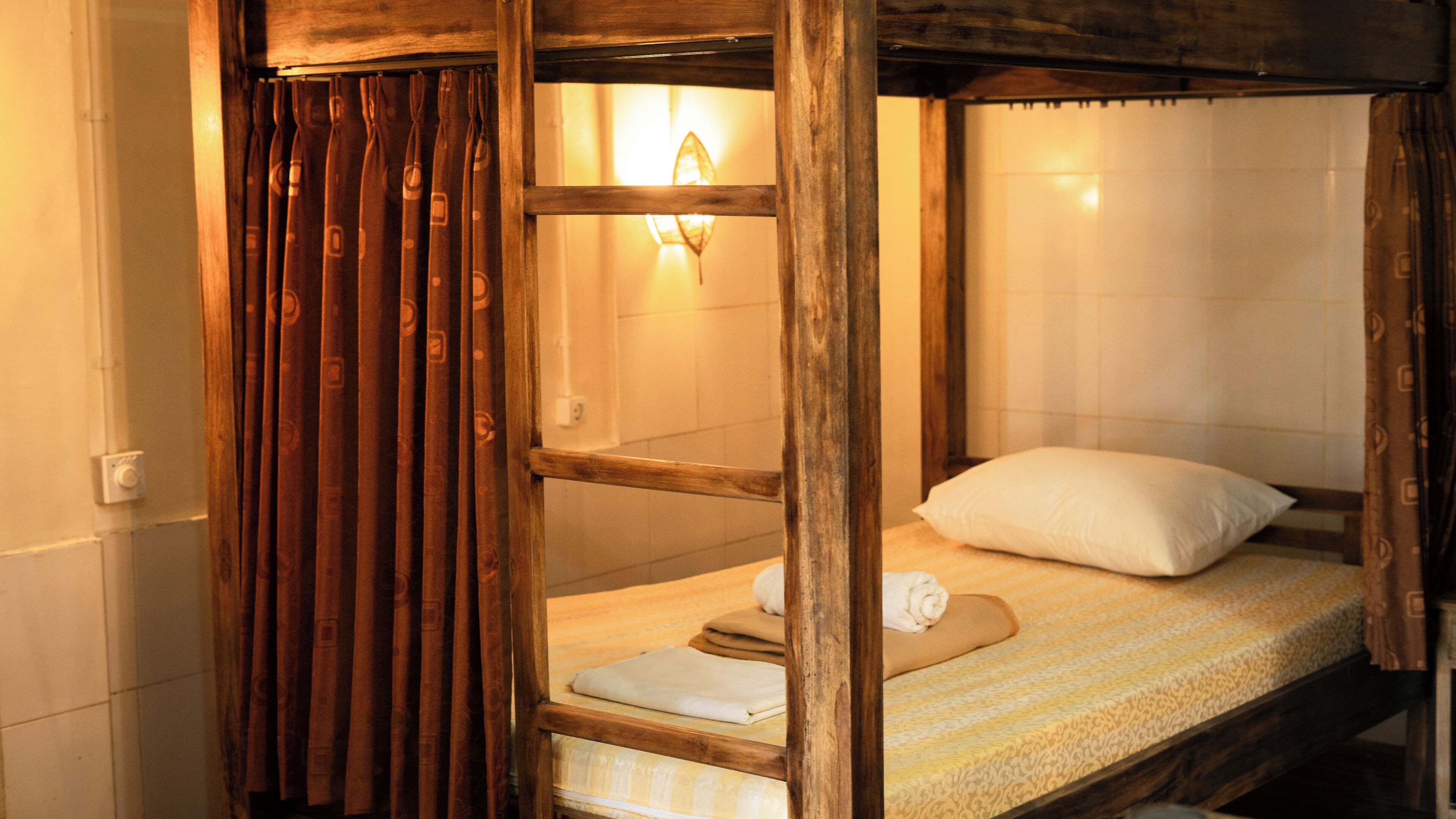 A rustic wooden bunk bed with a single white pillow and a folded towel.