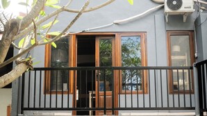 Un edificio de dos pisos con un balcón, una puerta de madera y un equipo de aire acondicionado.