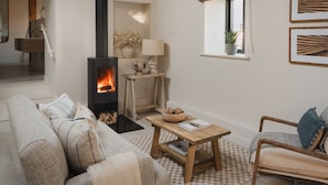 A cozy living room with a fireplace, a sofa, a coffee table, and a window with a plant.