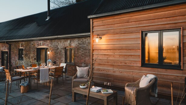 An outdoor patio with a wooden table, wicker chairs, and a brick wall.