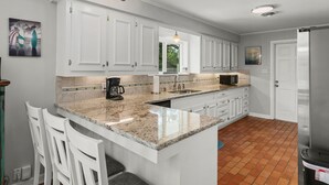 A modern kitchen with white cabinets, a granite countertop, a coffee maker, and a sink. - The Sea Glass House | Pet-friendly, Pool (Rockport)