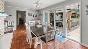 A dining area with a dark wooden table and white chairs, a chandelier, and a sliding glass door leading to an outdoor patio. - The Sea Glass House | Pet-friendly, Pool (Rockport)