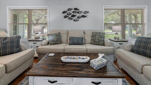 A living room with a beige sofa, two side tables with lamps, a wooden coffee table, and a ceiling fan. - The Sea Glass House | Pet-friendly, Pool (Rockport)