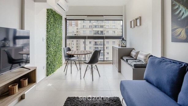 A modern living room with a flat-screen TV, a blue sofa, and a dining area with chairs and a table. - Apt in SP 600m From Allianz Parque - Tro0154 (São Paulo)