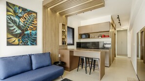 A modern living room with a blue sofa, a kitchen with a bar area, and a large tropical leaf artwork on the wall. - Apt in SP 600m From Allianz Parque - Tro0154 (São Paulo)