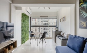 En moderne stue med et fladskærms-TV, en blå sofa og et spiseområde med stole og et bord.