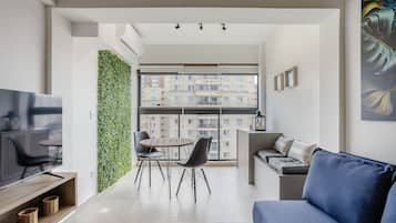 A modern living room with a flat-screen TV, a blue sofa, and a dining area with chairs and a table.