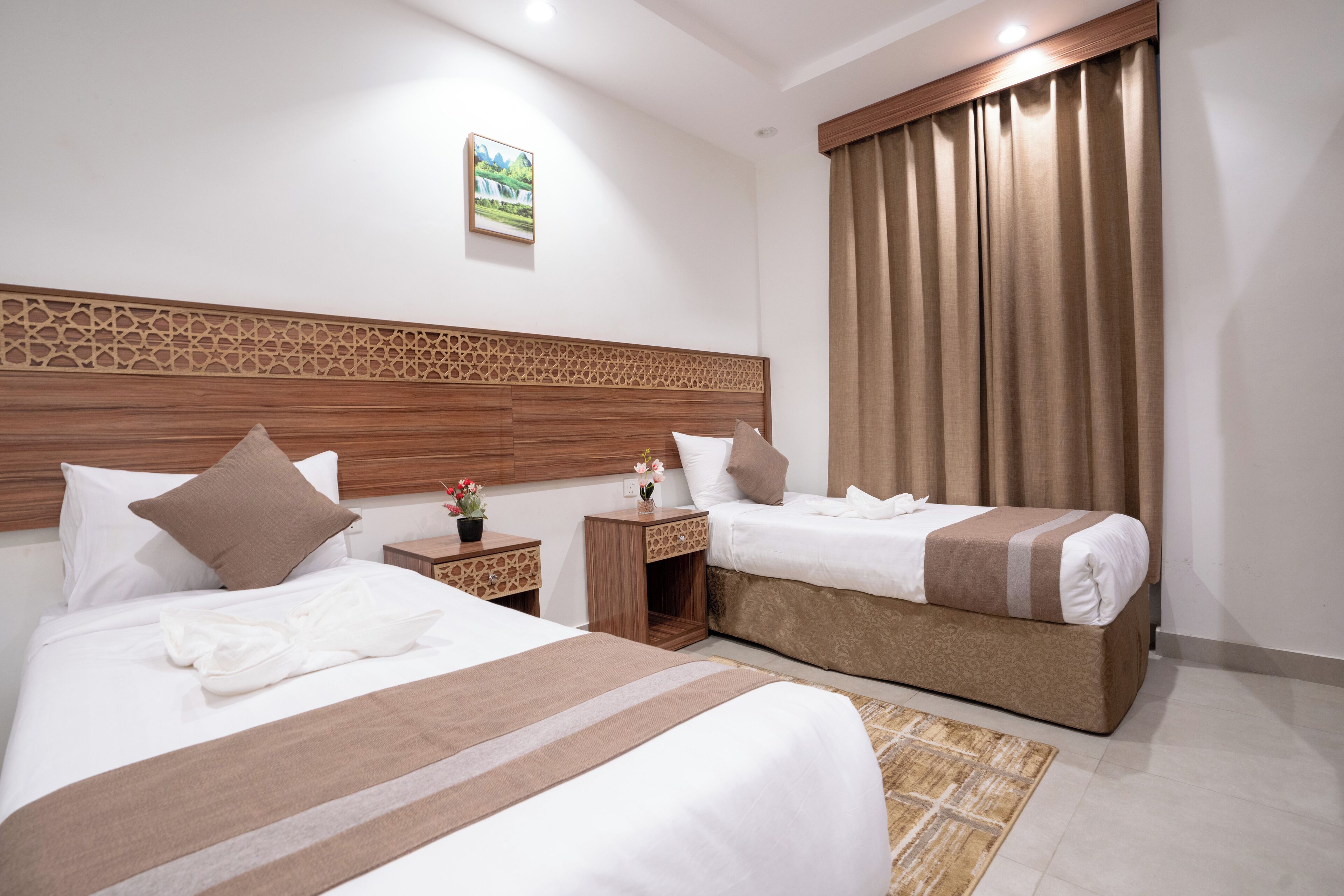 Une chambre d’hôtel avec deux lits, une tête de lit en bois, une petite table de chevet avec une plante et une grande fenêtre avec des rideaux.