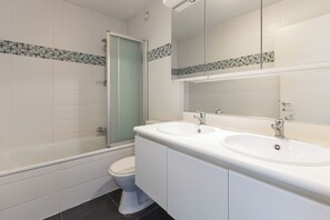 A modern bathroom with a glass-enclosed shower, a double sink vanity, and a toilet.