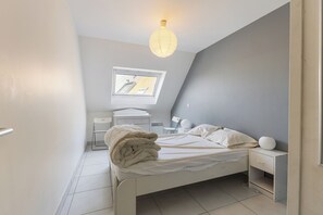 A bedroom with a bed, bedside table, lamp, and a window with a view of the outside.